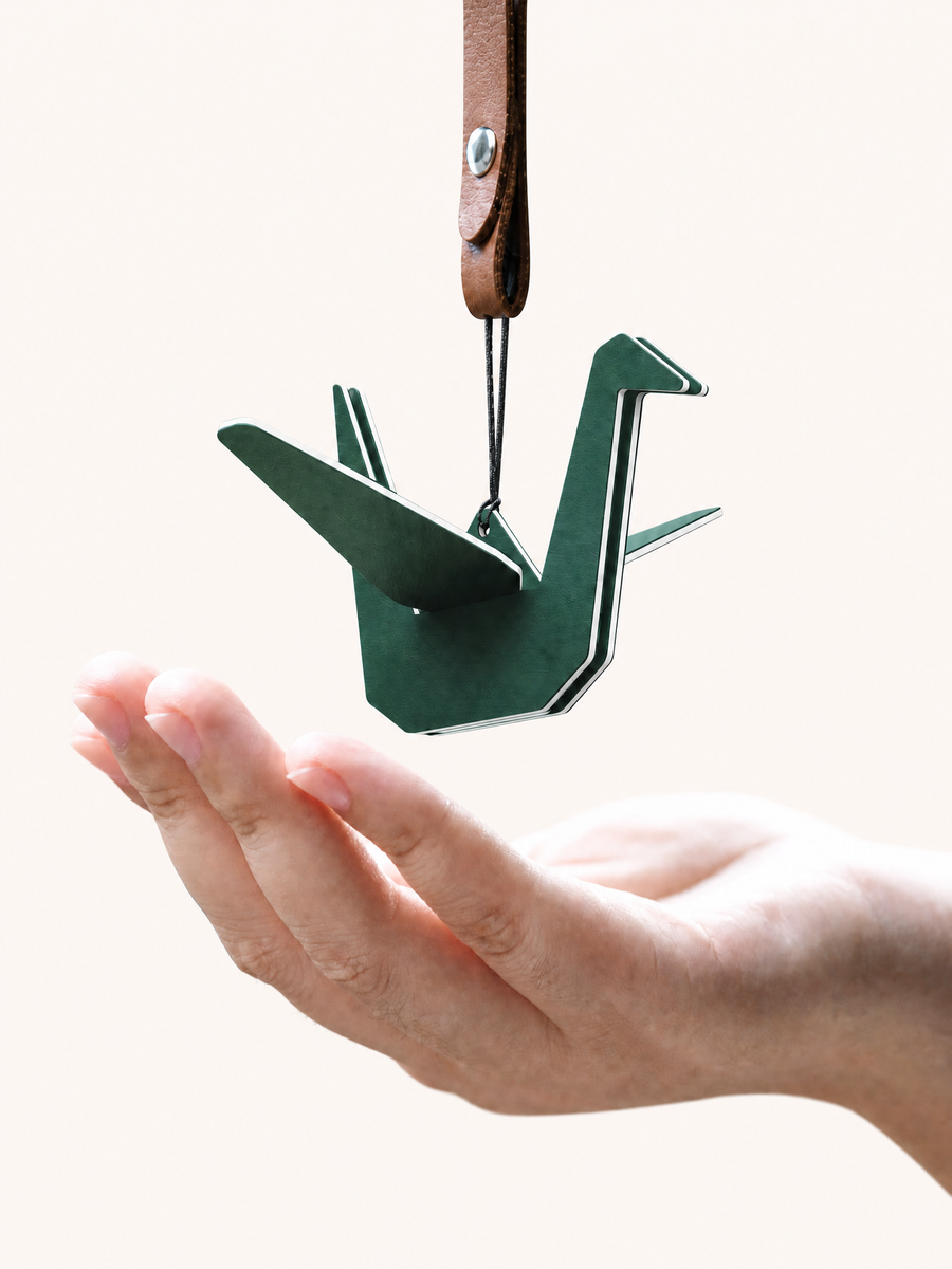 Hand holding green origami crane air freshener with brown leather strap
