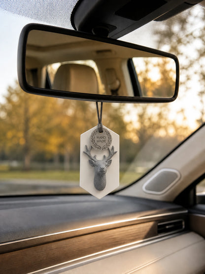 White-plaque gray stag medallion hanging below a rearview mirror in warm daylight