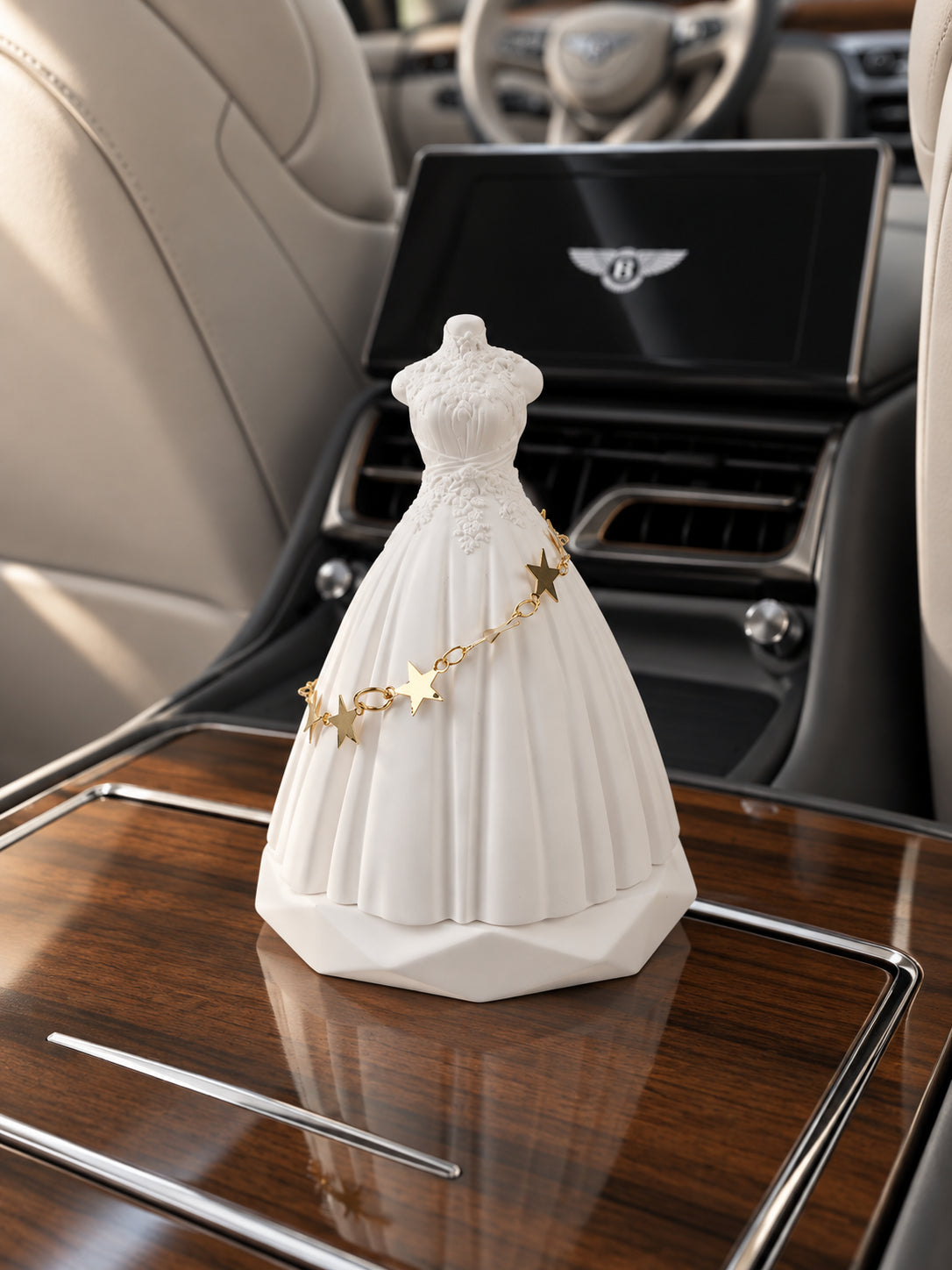 White bridal silhouette ornament on the closed rear-console wood lid of a parked Bentley Flying Spur