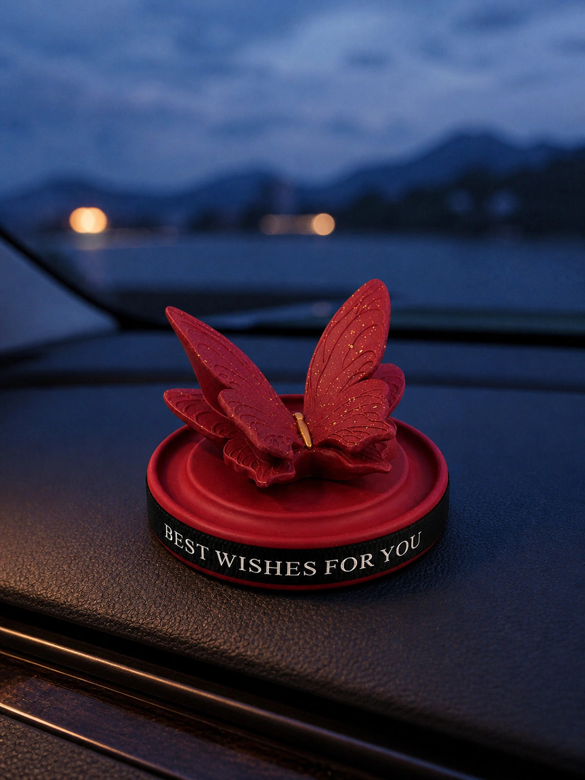 Burgundy Butterfly Dashboard Ornament resting on a vehicle dashboard at blue hour