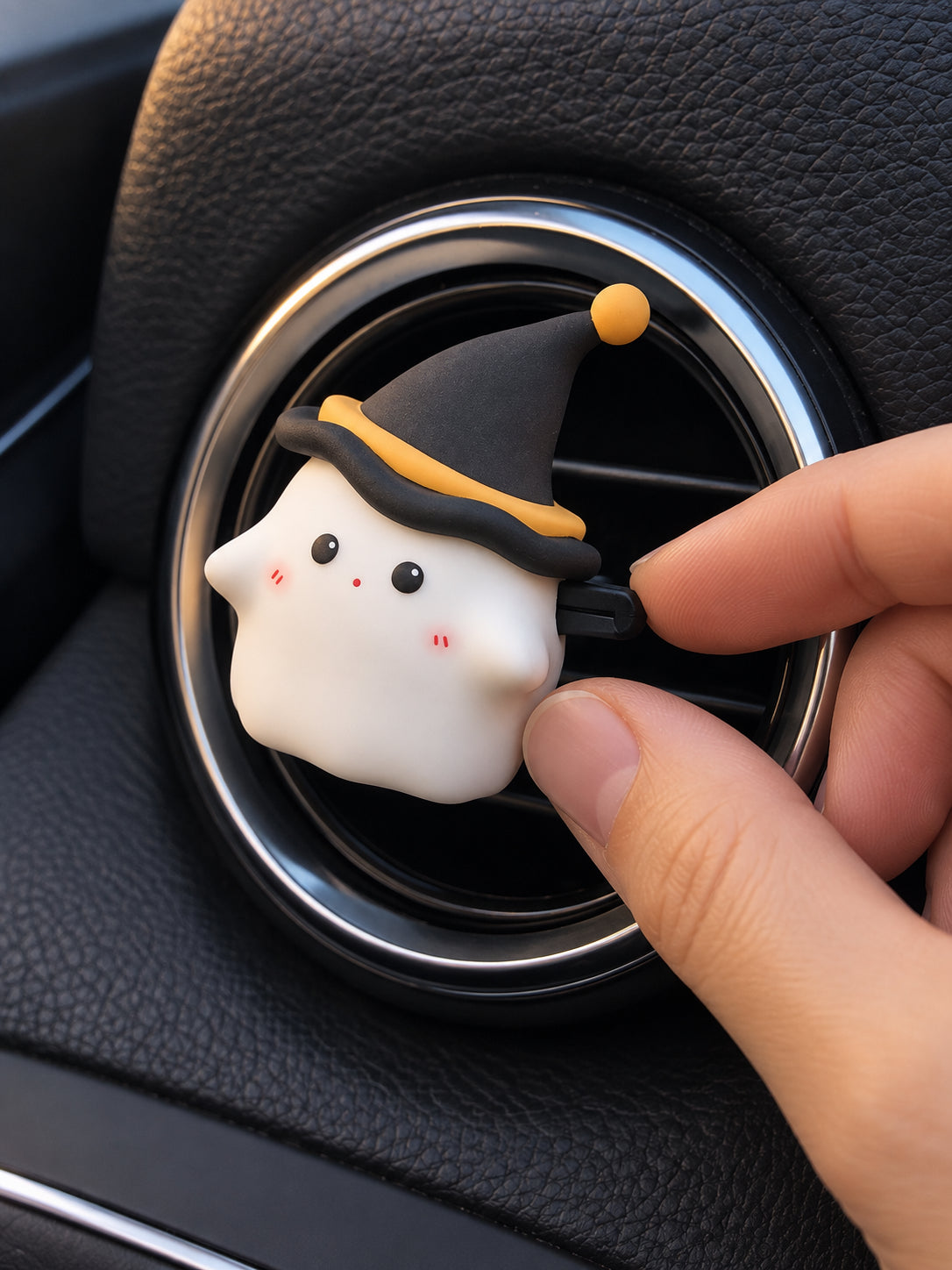 A hand gently steadies the Midnight Ghost ornament beside the adjustment tab of a round car vent