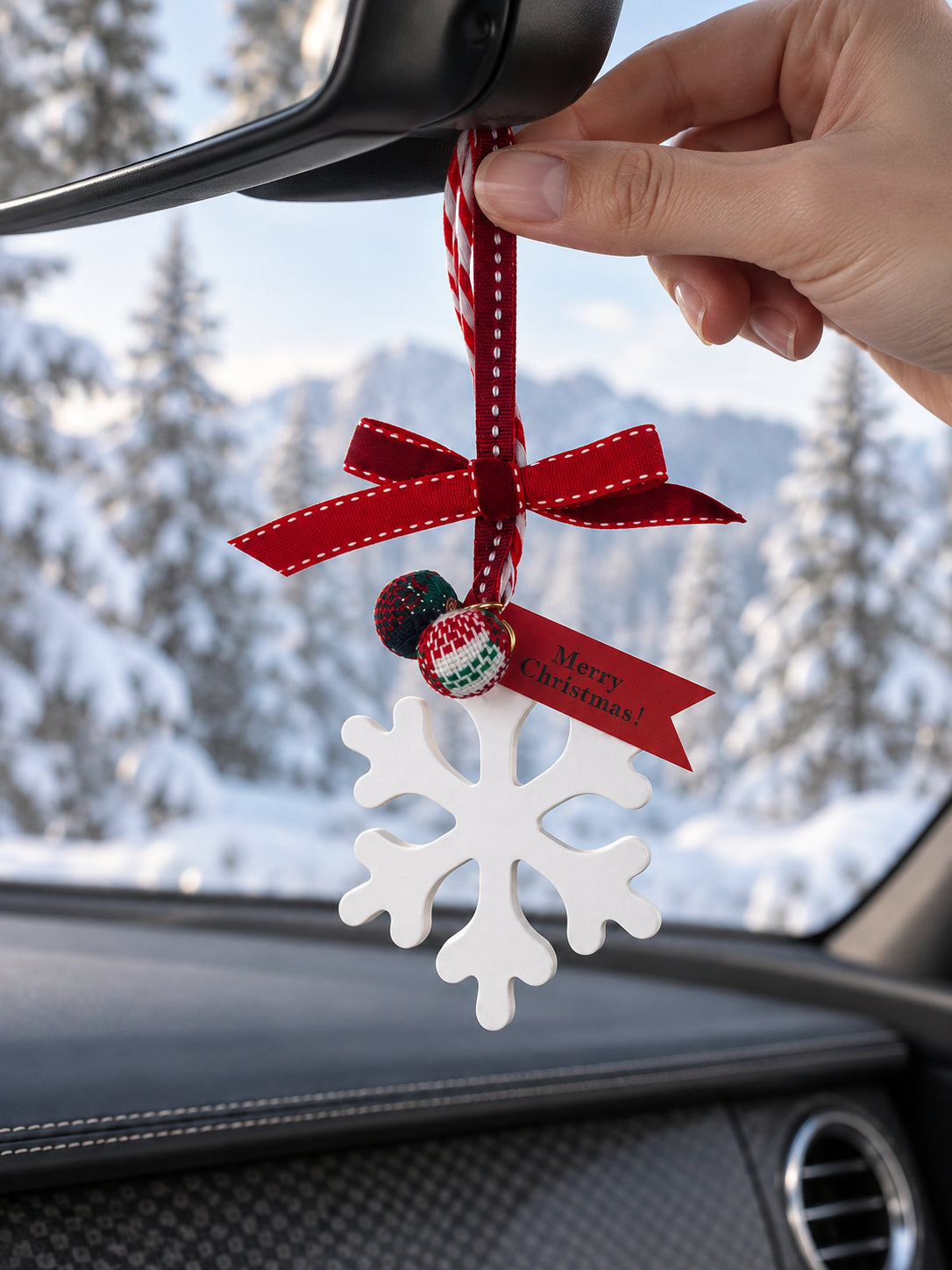A hand gently straightens the snowflake ornament ribbon beneath the rearview mirror while parked