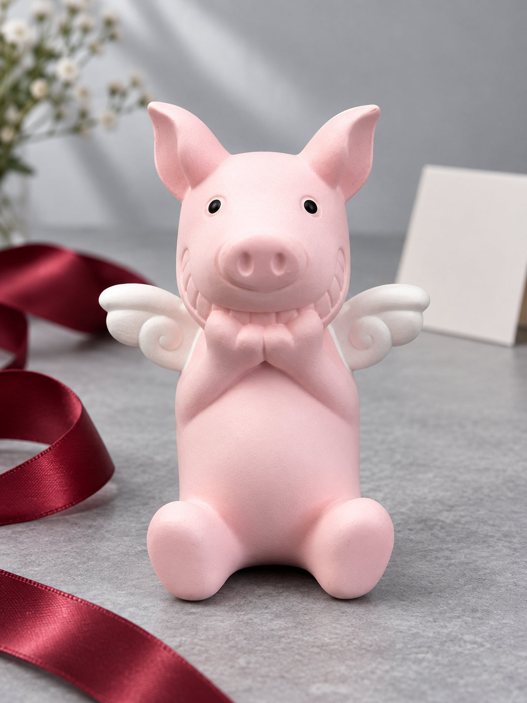 Pink angel-wing Wish Pig beside loose burgundy ribbon and a blank card; styling props not included