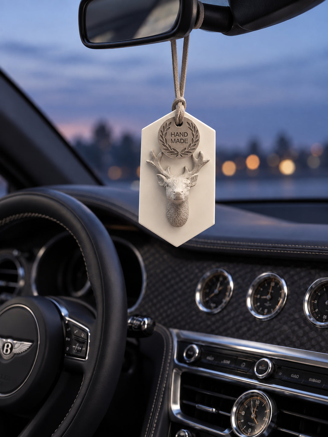 Gray stag medallion hanging from the mirror support in a parked Bentley Flying Spur at blue hour