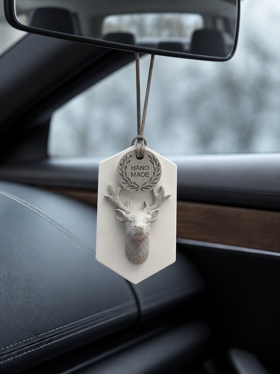 White plaque and gray stag ornament suspended on two gray cord strands below the rearview mirror